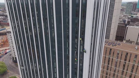 Drone approaching skyscraper with rope access window cleaners working on high Vidéo 334690382