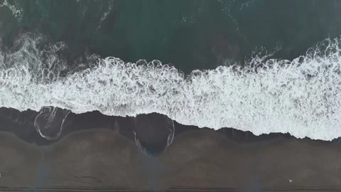 Drone ascending above powerful ocean wave breaking on black sand beach Video stock 337914733