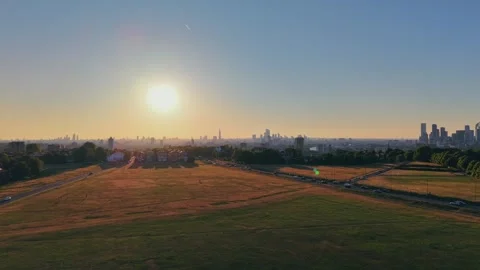Drone ascending over grassy park at golden hour with urban skyline Stock Footage 309769034