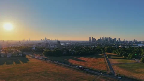 Drone ascending over grassy park at golden hour with urban skyline Stock Footage 309769050