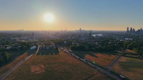 Drone ascending over grassy park at golden hour with urban skyline Stock Footage 309769097