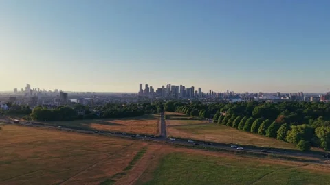 Drone ascending over grassy park at golden hour with urban skyline Stock Footage 309769174