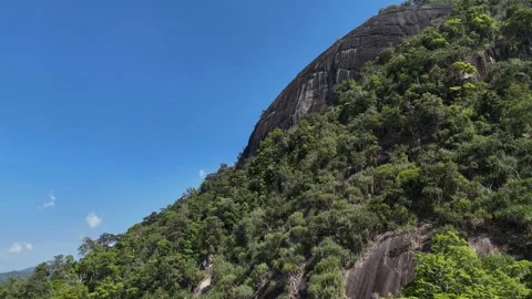 Drone ascending toward giant round rock atop forested mountain in Dak Lak 動画素材 336956183