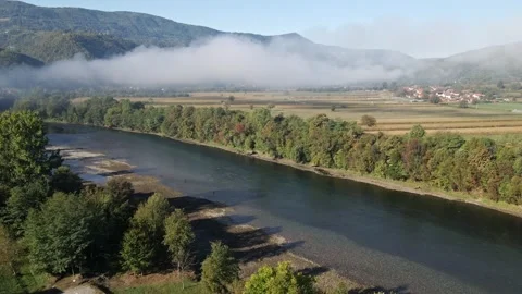 Drone ascends and captures a smoke over a river and cultivated fields in valley 動画素材 263059252