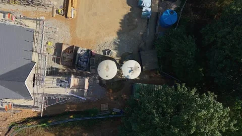Drone ascends top-down over cement silos on construction site beside forest Stock Footage 345669342