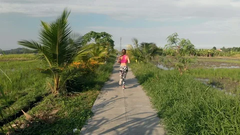 Drone back view follow the running girl on walking path among the rice field Stock Footage 129074712