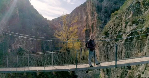 Drone backward flight recording an old man walking on a suspension bridge Stock Footage 124388368