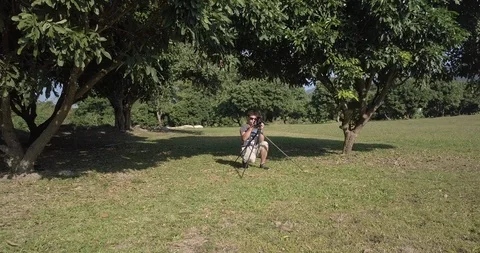 Drone backward shot with a man is taking video in park in choang mai Stock Footage 100746599