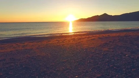 Drone begins to fly off the beach over the water surface to the sun Stock Footage 71765442