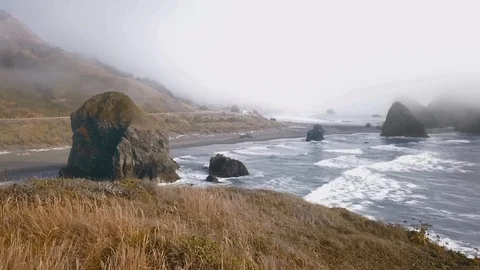 Drone camera approaches a hilly shore in the fog through cliffs in the water Video stock 123392085