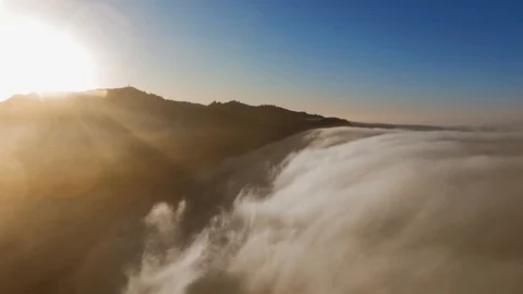 Drone camera flies over fluffy clouds and the top of the sunlit mountain (Malibu Vídeo Stock 126678767