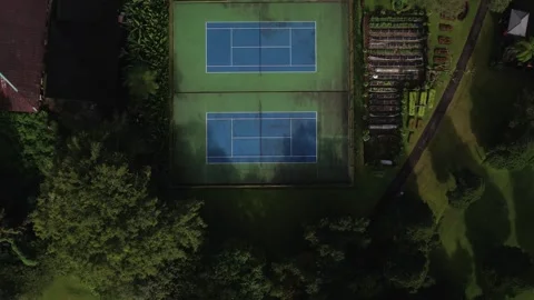 Drone camera flying down empty tennis court with green trees and house 스톡 동영상 247442994