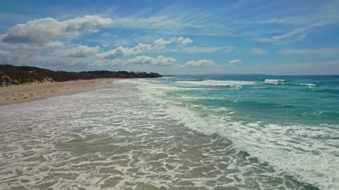 A drone camera glides over rolling ocean waves on a summer day, capturing a long Stock Footage 306123270