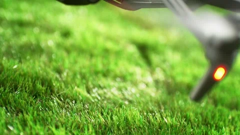 Drone With A Camera Mounted Ending Its Flight On Sunlit Green Grass - Close up Stock Footage 278831197