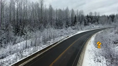 Drone camera moves along a highway with a yellow sign in a pine winter forest Video stock 119236952