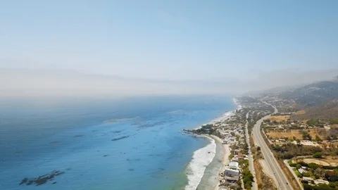Drone camera shoots cloudy horizon, blue ocean, coastal settlement, winding road Video stock 126676179