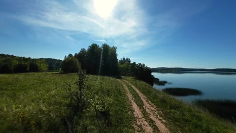 A drone captures a scenic path leading to a calm lakeside under a bright Видео 282735060