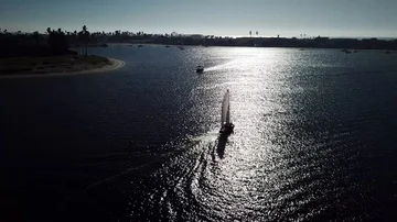 Drone chases small white sailboat in sun reflection on Mission Bay Stock Footage 86128989