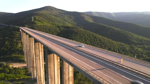 Drone chasing speeding car on viaduct highway bridge against green hills at Stock Footage 206036573