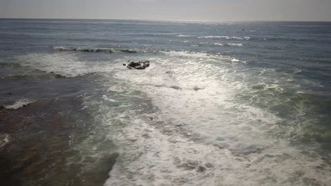 Drone circles over surfers near a huge rock as they paddle out and catch waves Stock Footage 97164341