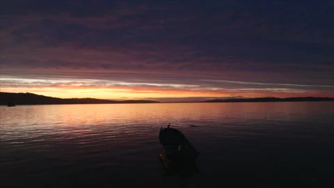 Drone circling small boat in middle of water at sunset 動画素材 340995445
