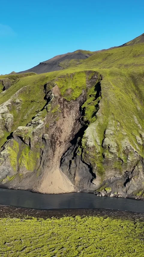 Drone close-up of moss-covered volcanic cliff with rockfall scar dropping into Stock Footage 328991374