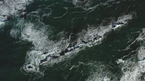 Drone decreasing over waves crashing into a grouping of rocks protruding Video stock 104812435