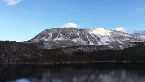 Drone Descends Toward Mirror-Dark Alpine Lake Below Snow-Streaked Mountain Vídeos de archivo 336220941