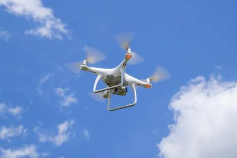 Drone DJI Phantom 4 in flight. Quadrocopter against the blue sky with white.. Stock Photos