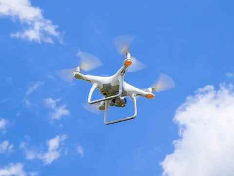 Drone DJI Phantom 4 in flight. Quadrocopter against the blue sky with white c Stock Photos