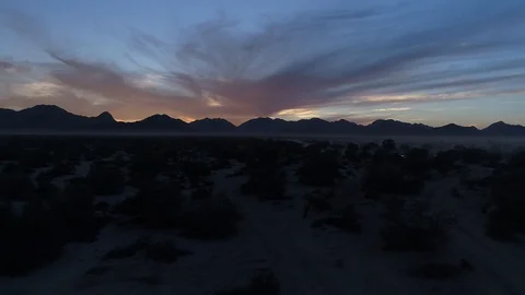 Drone dusk, back lit mountains and desert with dirt bike in crossing frame Stock Footage 104884051