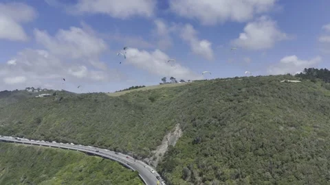 Drone facing east rises up over coastal highway with paragliders above Stock Footage 326769781