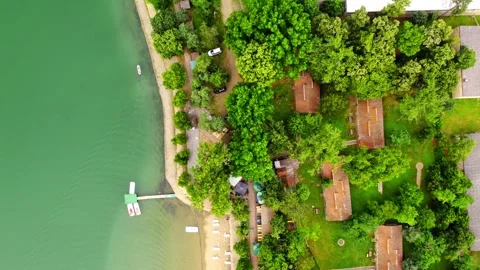 Drone flies above lakeshore capturing small pier, green trees and small houses Stock Footage 269165251