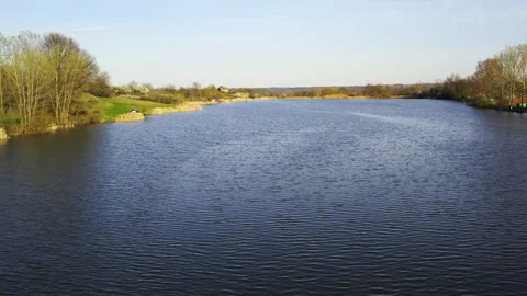 Drone flies above rippling surface of clear blue lake and land surrounding it Stock Footage 262750486