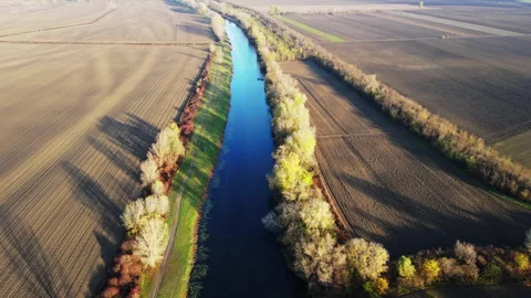 Drone flies above a river surrounded with empty agricultural fields and trees Stock Footage 263205213