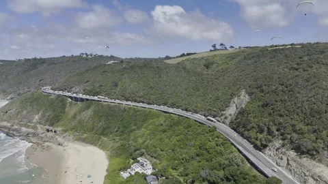 Drone flies along beach next to coastal highway above waves crashing the shore Video stock 326750139
