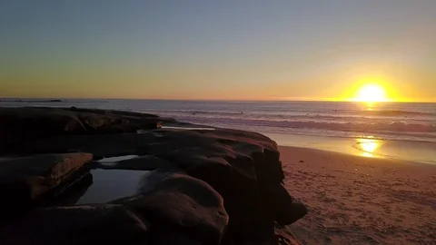 Drone flies around huge boulder to reveal stunning beach at sunset Stock Footage 100867250