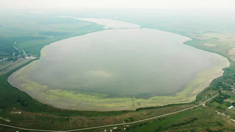 Drone flies around large round lake near village in cloudy day Stock Footage 263308388