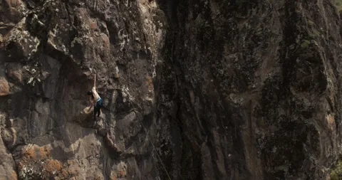 A drone flies around a young athletic female climber hanging on one arm on a Stock Footage 255877684