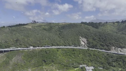 Drone flies backwards from forested hill with sky full of paragliders Stock Footage 326749983