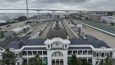 Drone flies backwards from front of train station with large suspension bridge Stock Footage 333842126