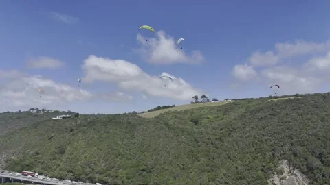 Drone flies backwards from hill with paragliders floating above Stock Footage 326764101