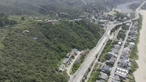 Drone flies backwards looking down at paragliders over coastal highway Stock Footage 326769787