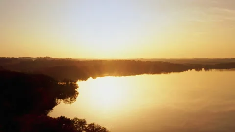 A drone flies backwards over a lake as the sun rises. The landscape is reflected Stock Footage 239100920