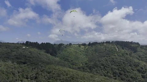 Drone flies backwards as paragliders float over forested hills on a sunny day Stock Footage 326702450