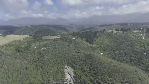 Drone flies backwards from paragliders over forested hill Stock Footage 326769651