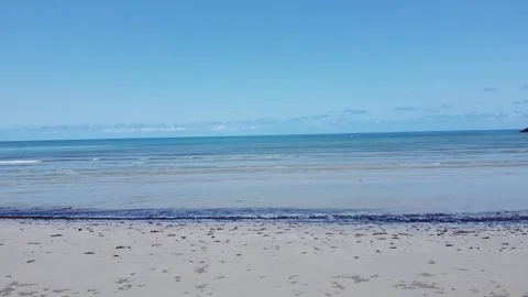 A drone flies from a beach shore over the water and the calm waves Stock Footage 135492575