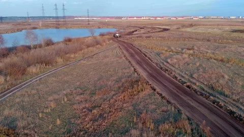 The drone flies behind a tractor by a grader that levels a country road among Stock Footage 164715174