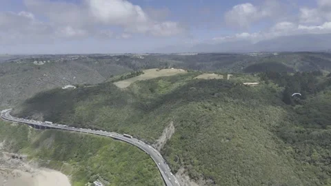 Drone flies east high over coastal highway with paragliders above Stock Footage 326769773