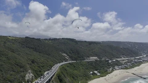Drone flies east over beach, highway, and forested hill with paragliders Stock Footage 326750154